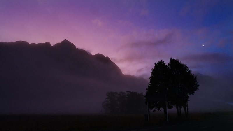 A mountain range is silhouetted against a purple sky at dusk.
