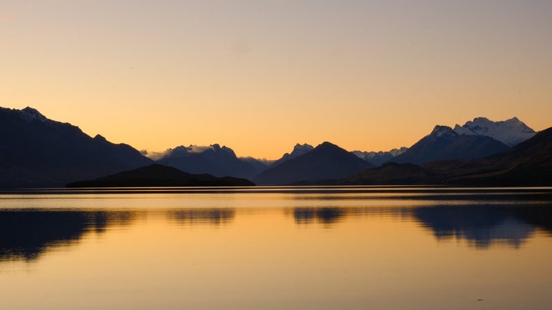 A serene lake scene with mountains in the background, reflecting off the water's surface.