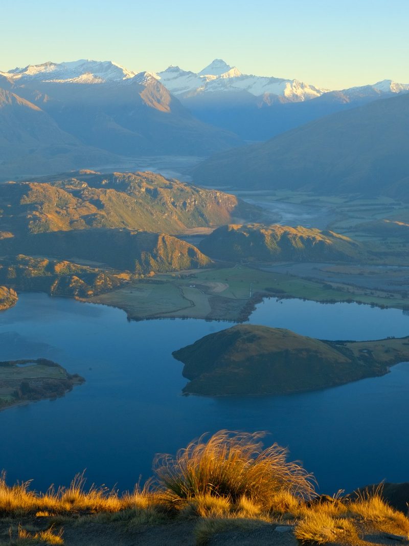 A serene landscape featuring a lake, mountains, and grassy hills under a clear blue sky.