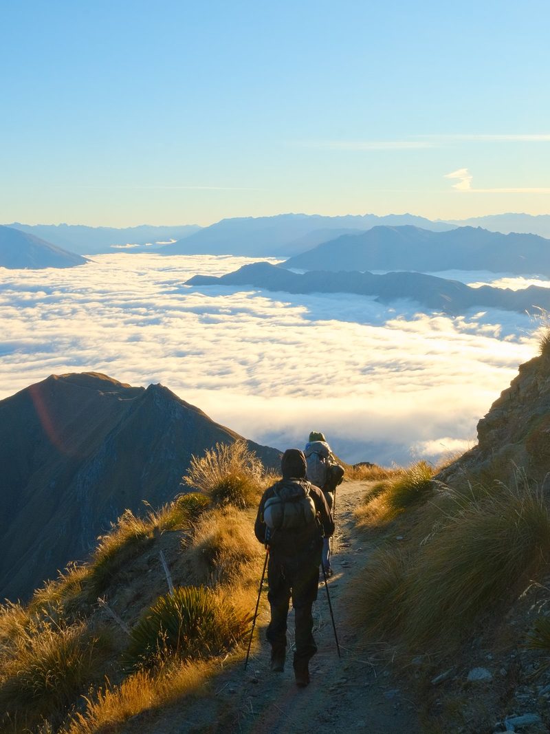 Two people hiking on a mountain trail above the clouds.