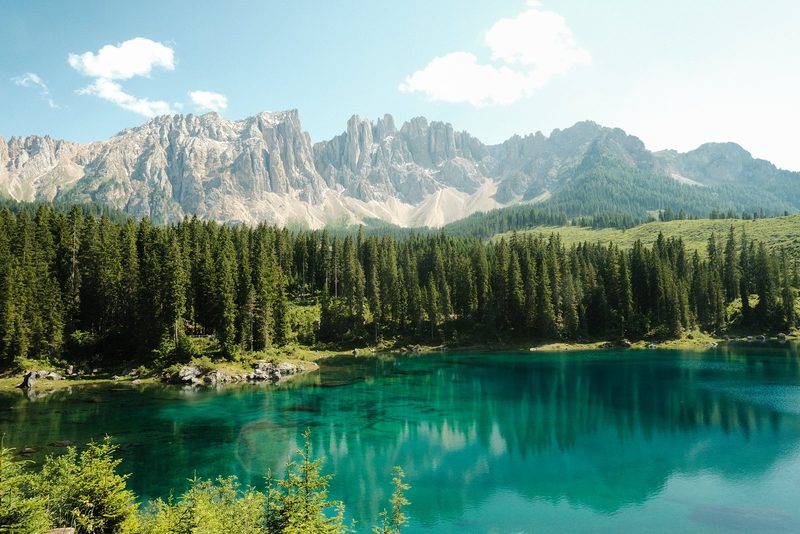 A serene landscape featuring a large body of water, surrounded by lush greenery and majestic mountains in the distance.