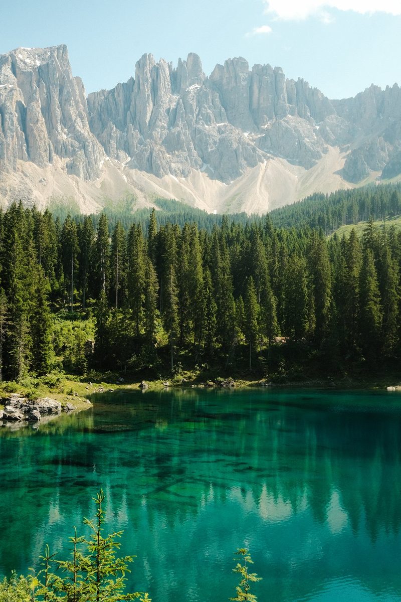 A serene landscape featuring a tranquil lake, surrounded by lush trees and majestic mountains under a clear blue sky.