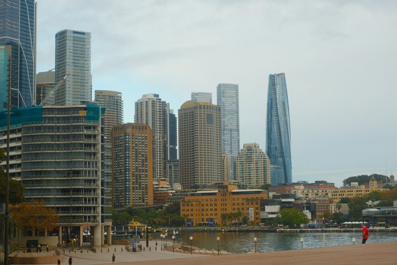 A city skyline with a river running through it, featuring a mix of tall buildings and a cloudy sky.