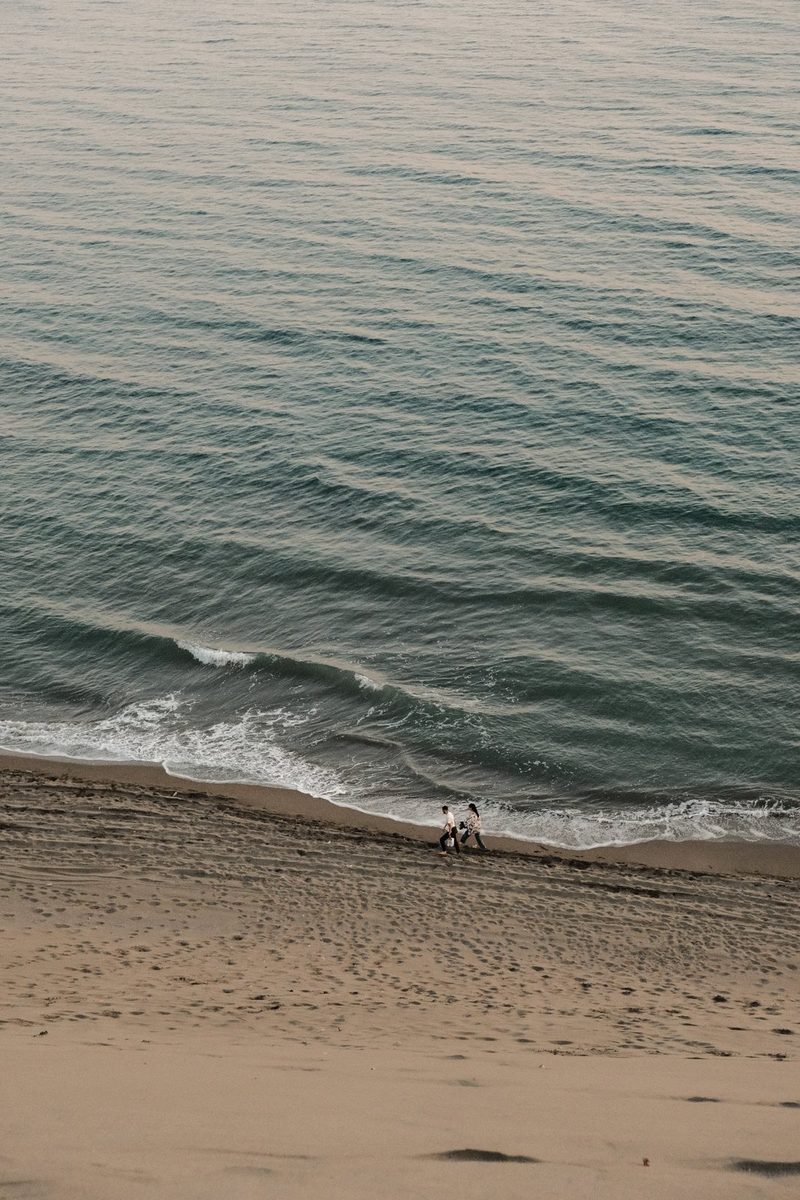 A beach with a large body of water and two people walking along the shore.