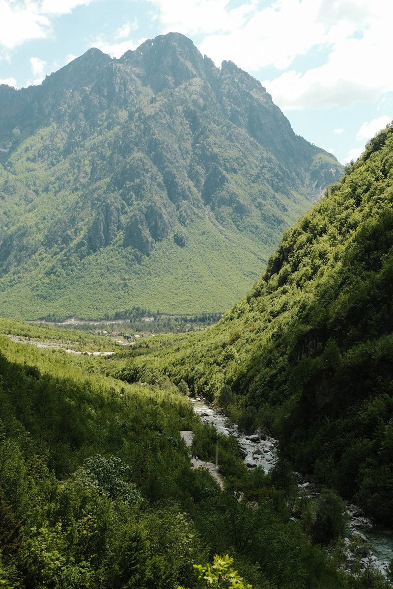 A mountainous landscape with a river running through it, surrounded by lush greenery.