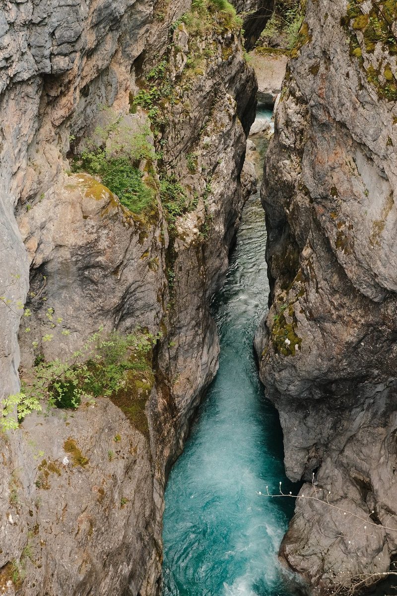 A narrow river flows between two rocky cliffs, surrounded by lush greenery.