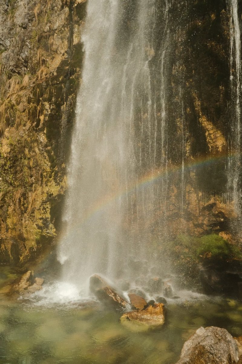 A waterfall cascades down a rocky cliff, surrounded by a rainbow in the mist.
