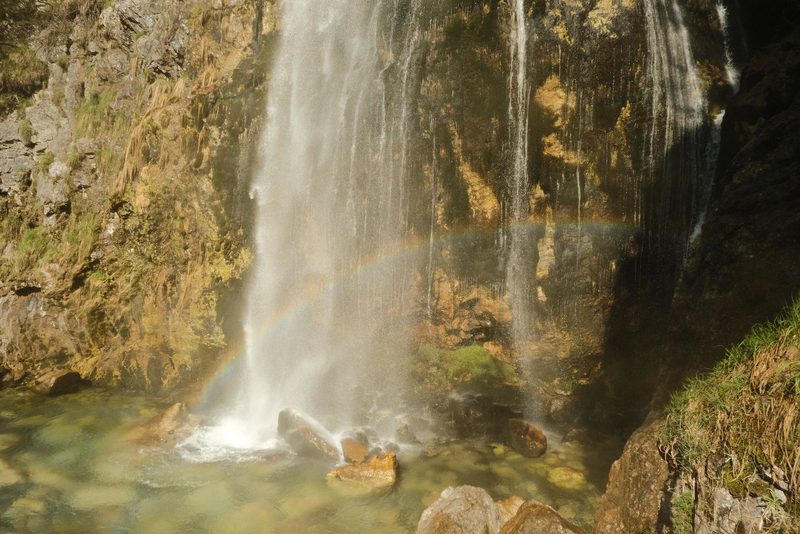 A waterfall cascades into a pool of water surrounded by rocks and vegetation.