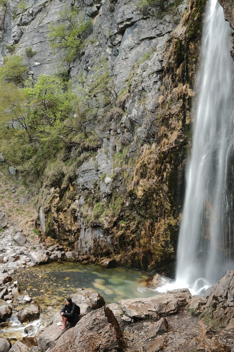 A waterfall cascades down a rocky cliffside, surrounded by lush greenery and a serene pool at its base.