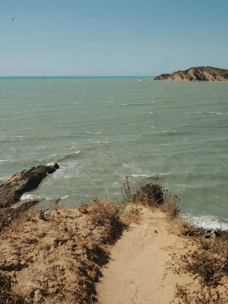 A sandy path leads down to a rocky shoreline, where the sea meets the land.
